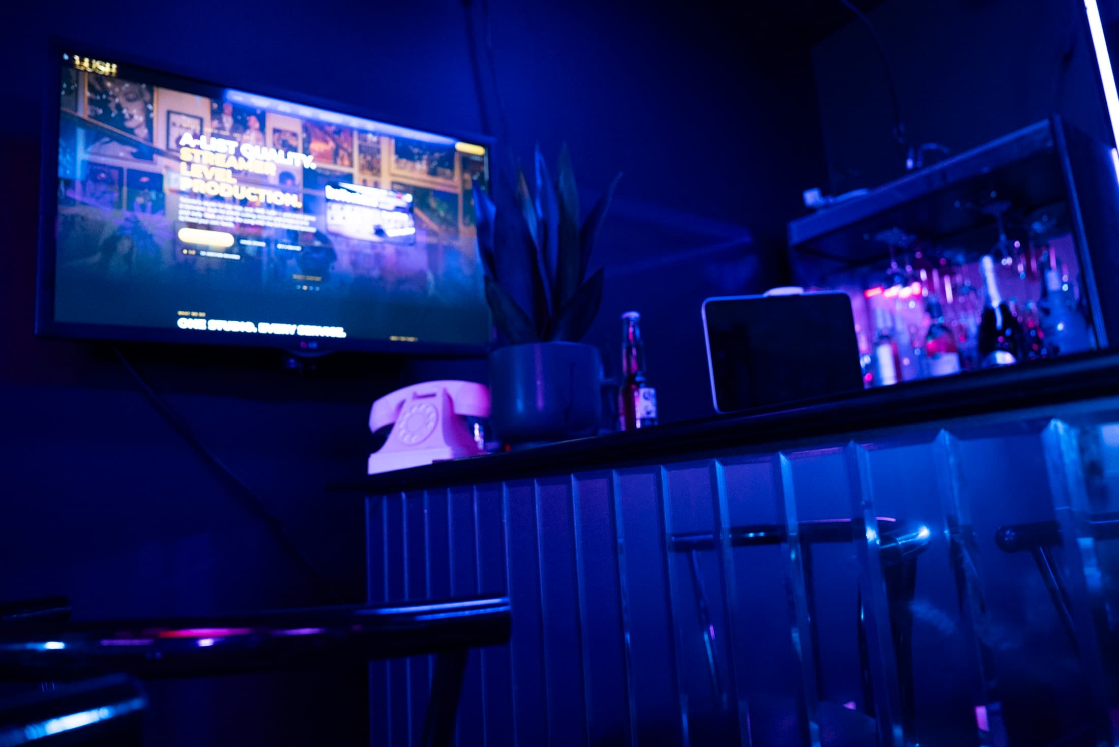 Bar top at Lush Event Space — screen content, pink rotary phone and backlit spirits shelf in blue light