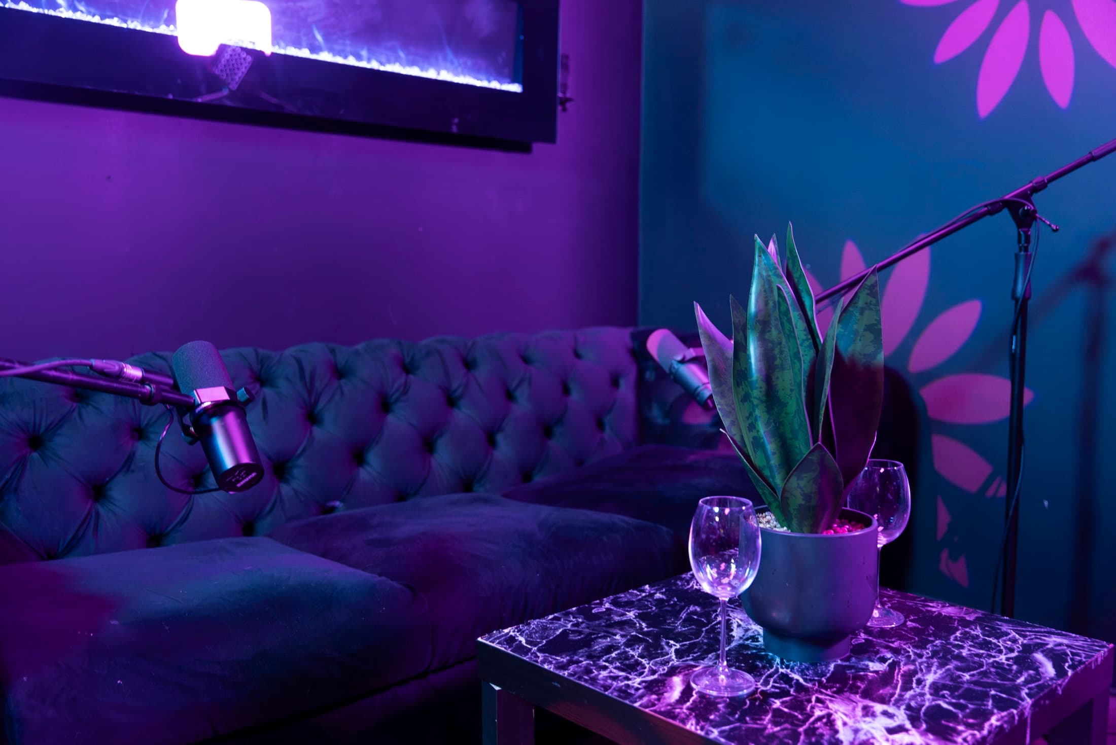 Detail of the podcast sofa corner — microphone, fireplace light, marble side table with wine glasses