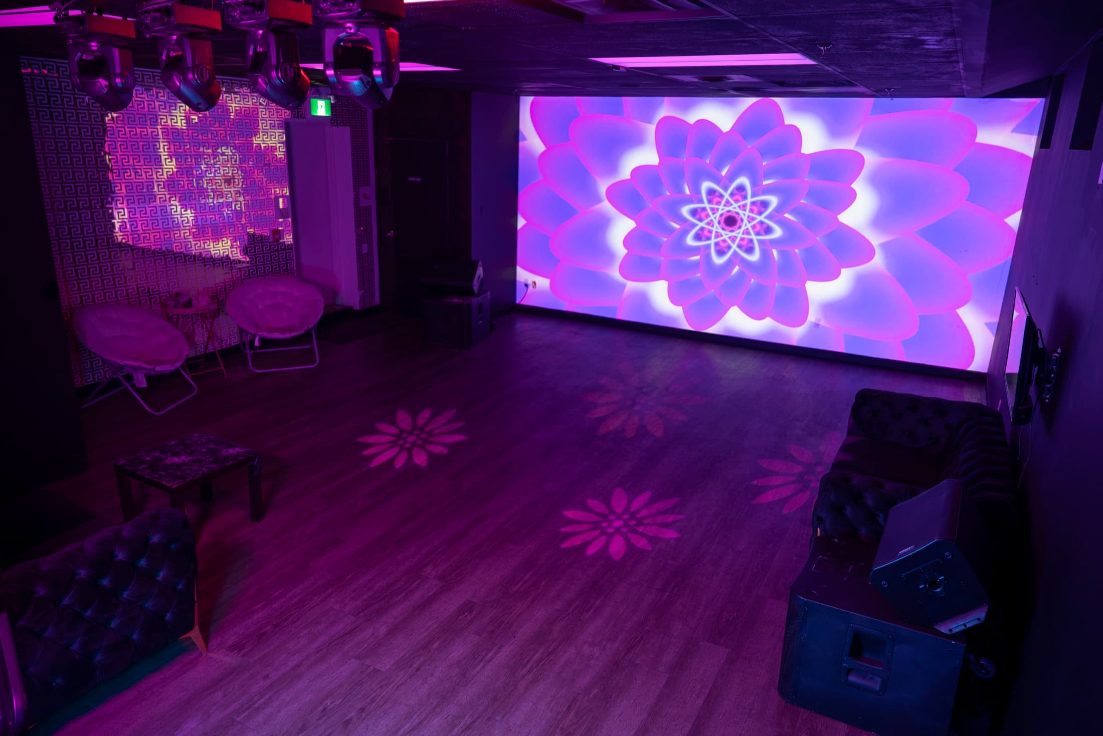The 20ft projection wall at Lush Event Space — full-wall flower visuals over the dance floor, moving-head lights above, matching floral light patterns on the floor and Versace accent wall